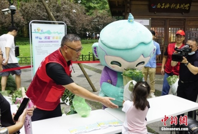 杭州亚运会吉祥物“琮琮”“宸宸”“莲莲”在浙江杭州西湖畔参加莲蓬荷叶义卖活动,图为亚运会吉祥物“莲莲”将分包好的莲蓬、荷叶交给顾客。<a target='_blank' href='/'><p align=