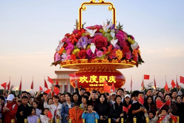 2025年10月1日,在北京天安门广场,人们观看升国旗仪式后挥舞国旗。